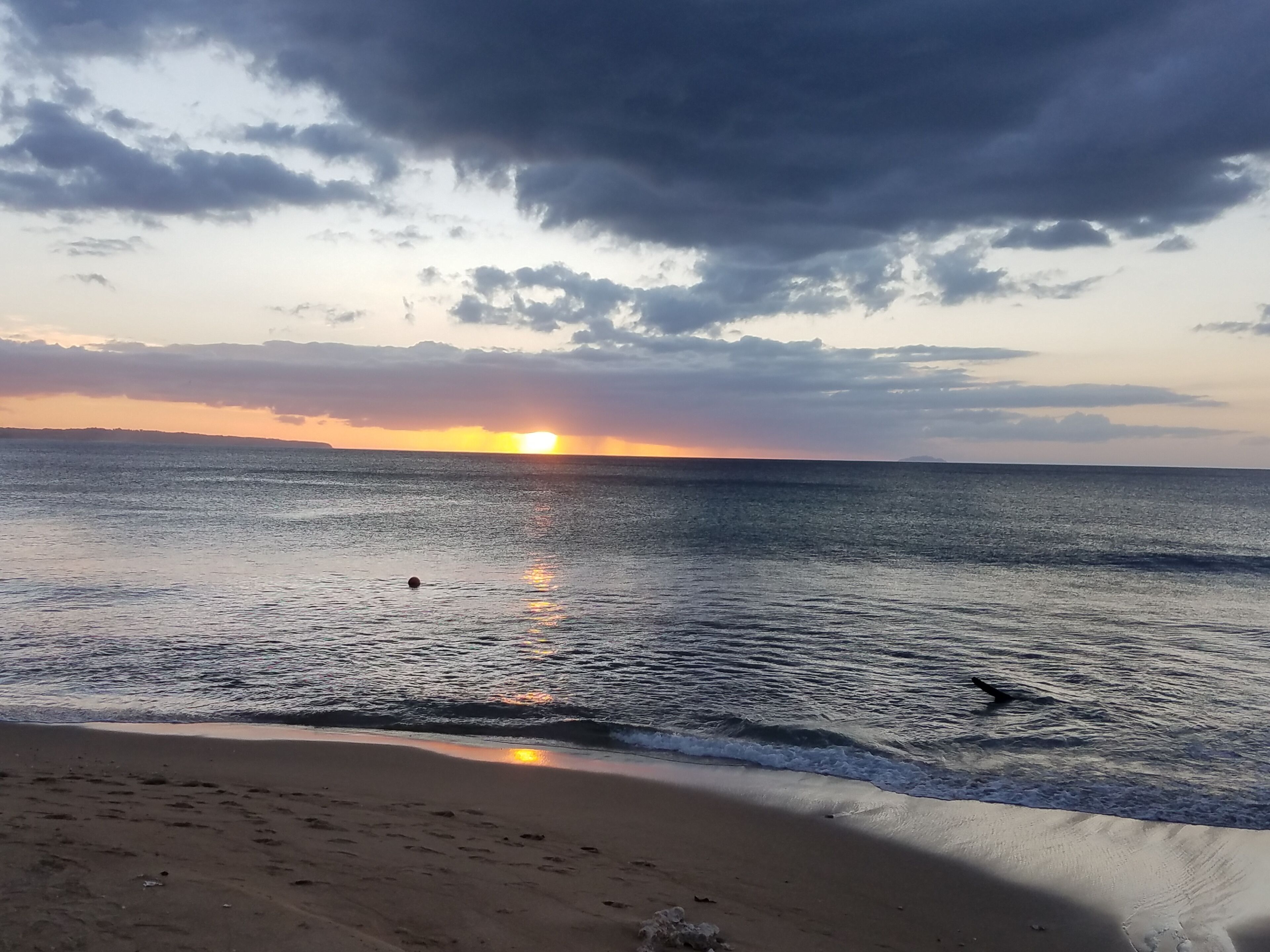 A beach with a sunset, calm sea, and footprints in the sand.