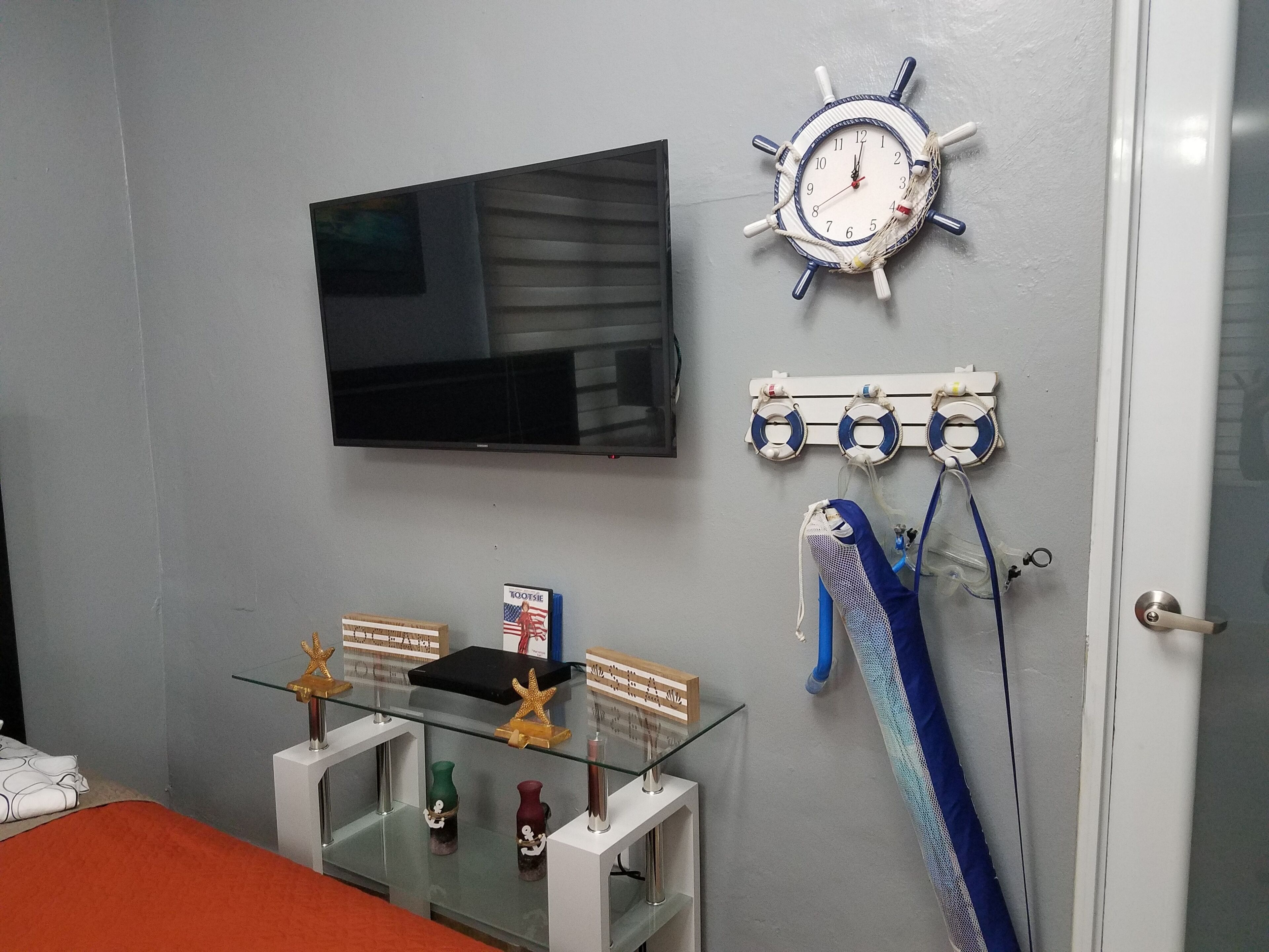 Una habitación con un televisor montado en la pared, un reloj, salvavidas y una vitrina de vidrio con objetos decorativos.