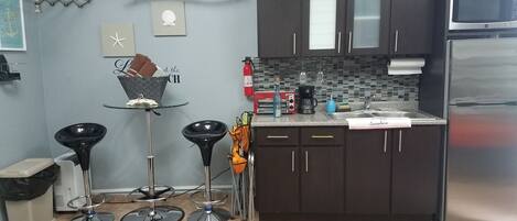 A compact kitchen with dark cabinets, a stainless steel refrigerator, and a tiled backsplash.