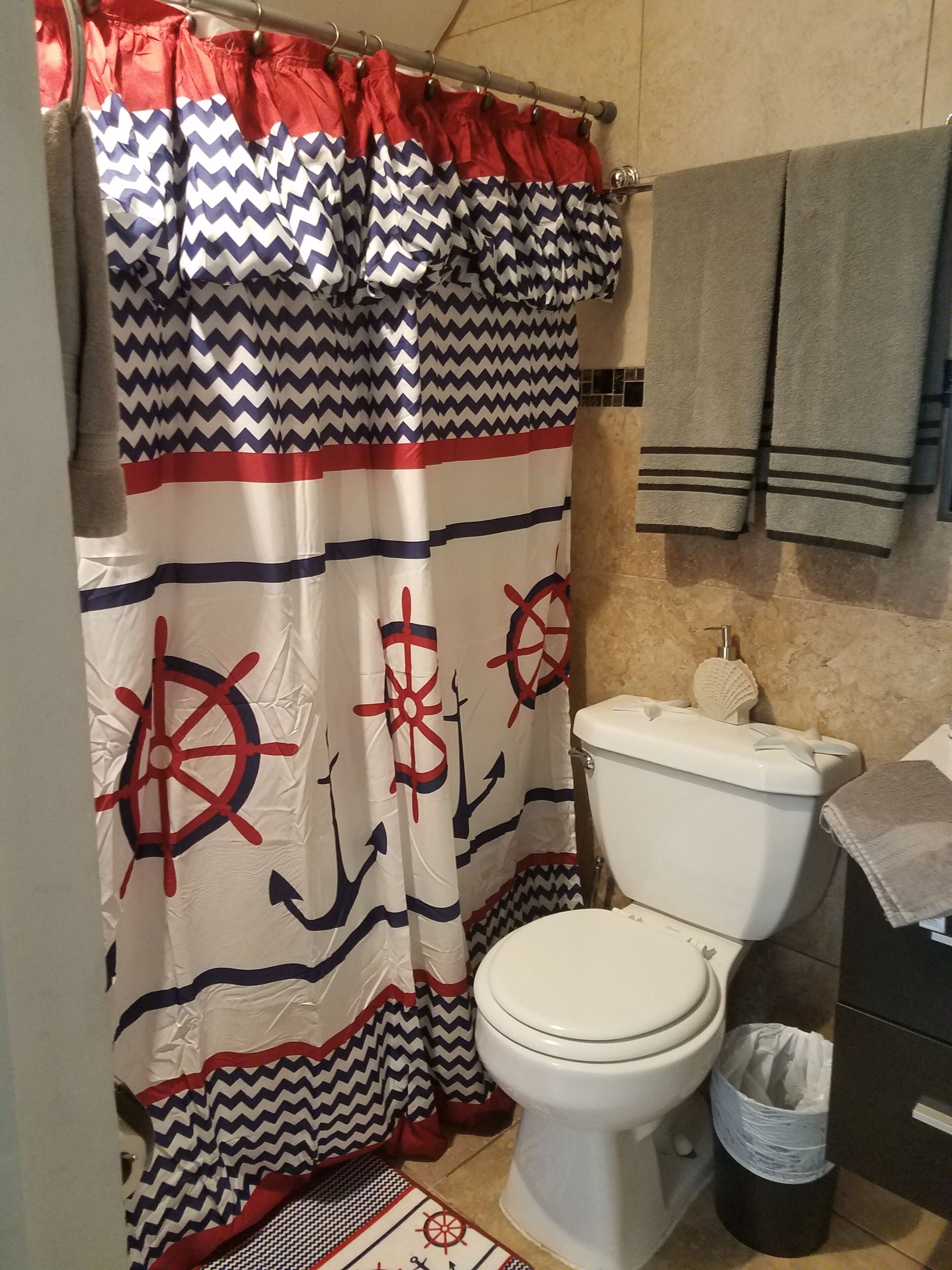 Un baño con cortina de ducha de temática náutica, inodoro y cubo de basura.