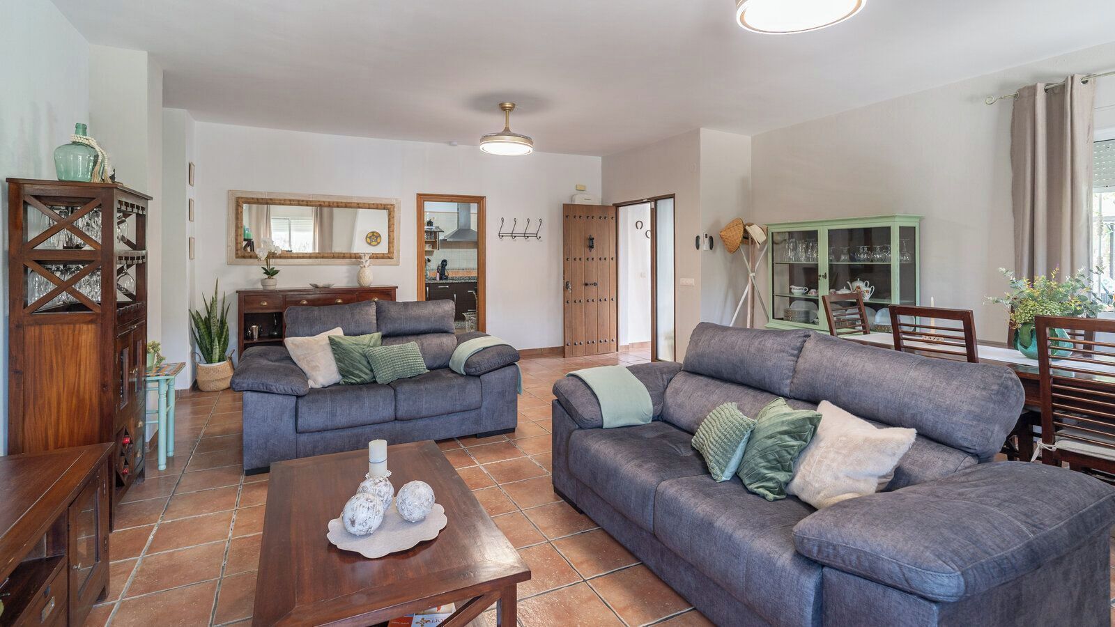 Un salon avec deux canapés gris, une table basse en bois et un coin repas comprenant un buffet vert et des chaises en bois.