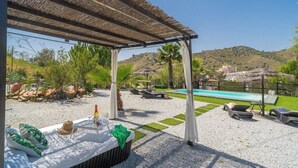 Ein überdachter Außenbereich mit Pool, Palmen und Blick auf Hügel.