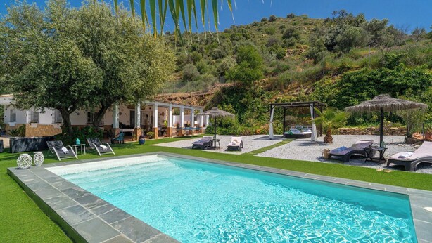 Ein Pool mit Liegestühlen, einer Pergola und einer Hügelkulisse.