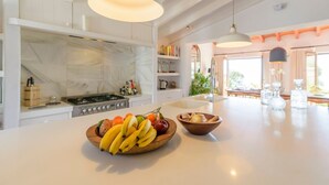 A modern kitchen with a large island, white cabinetry, and a central island with a bowl of fruit and vegetables. - The Hunting Lodge Alcaucín by Ruralidays (Málaga)