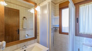 Un bagno con lavandino, specchio, doccia e finestra.