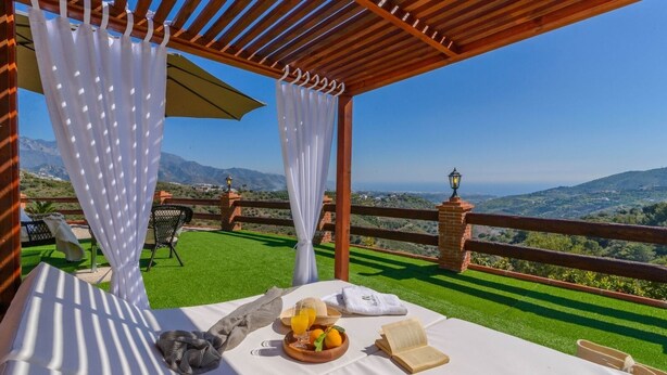 Una terraza con mesa preparada para el desayuno, vista al campo y una estructura de pérgola.