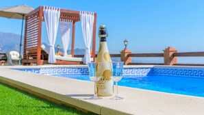 Una botella de champán y dos copas junto a una piscina, con vistas despejadas a la piscina y montañas al fondo.
