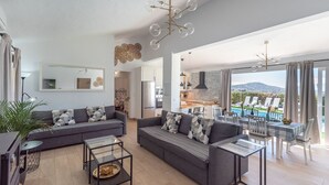 A modern living room with grey sofas, a glass coffee table, and a view of a pool and mountains. - Cortijo Entre Pueblos Cómpeta by Ruralidays (Málaga)