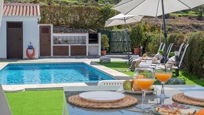 A poolside area with a swimming pool, lounge chairs, umbrellas, and a table set for a meal. - Cortijo Entre Pueblos Cómpeta by Ruralidays (Málaga)