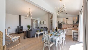 A spacious living area with a fireplace, a dining table set for four, and a kitchen with modern appliances. - Cortijo Entre Pueblos Cómpeta by Ruralidays (Málaga)
