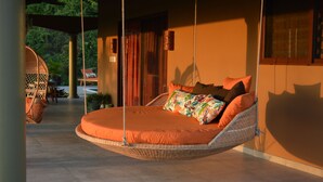 Ein Hängebett mit orangefarbener Bettwäsche in einem hellen Raum mit Blick auf Grünflächen.