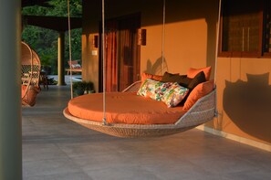 A hanging bed with orange bedding in a well-lit room with a view of greenery outside.