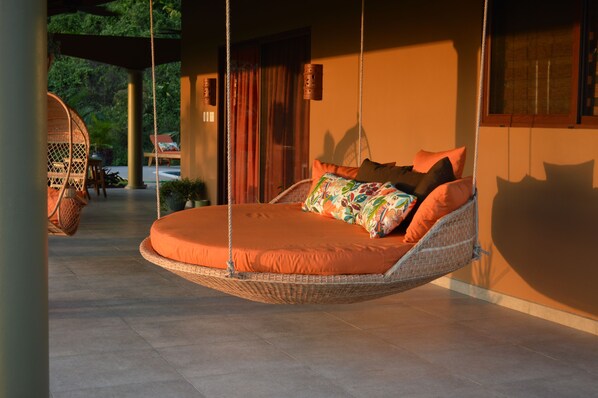 A hanging bed with orange bedding in a well-lit room with a view of greenery outside.