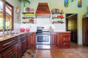 A kitchen with wooden cabinets, a stainless steel stove, and various kitchenware on shelves. - Casa de las Mariposas-Where Jungle Meets the Sea (San Buena)