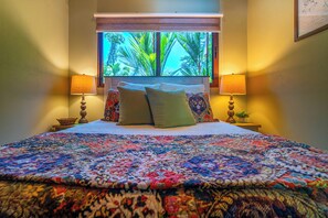 A bed with a colorful quilt, two bedside lamps, and a window with a view of palm trees. - Casa de las Mariposas-Where Jungle Meets the Sea (San Buena)