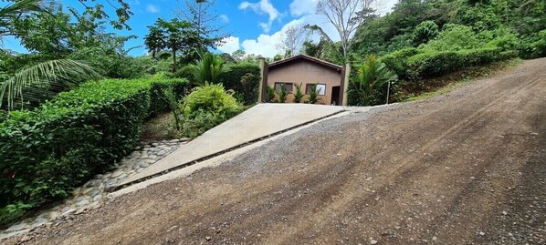 A dirt road leading to a small building surrounded by lush greenery.