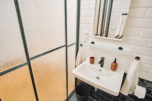A bathroom with a white sink, a mirror, and a black trash bin. - CAMŌ ROOMS - Boutique Aparthotel (Prague)