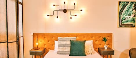 Quarto de hotel bem organizado com uma cama grande, luminária fixada na parede e uma obra de arte emoldurada.