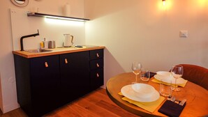 A compact kitchen with a sink, cabinets, and a countertop. There is a dining table with plates, glasses, and cutlery. - CAMŌ ROOMS - Boutique Aparthotel (Prague)