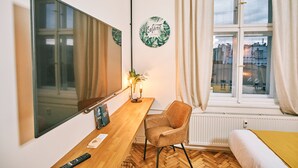 A room with a wooden desk, a chair, a large mirror, a window with curtains, and a wall with a circular sign. - CAMŌ ROOMS - Boutique Aparthotel (Prague)
