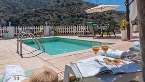 A poolside area with a pool, lounge chairs, and a table with drinks and a newspaper.