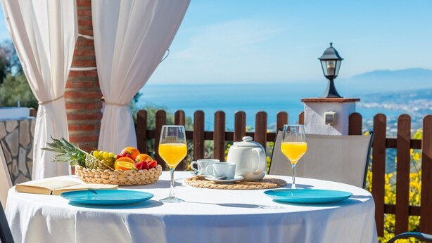 A table set for breakfast with a view of the sea, a basket of fruit, and two glasses of orange juice. - Villa Francisco Torrox by Ruralidays (Málaga)