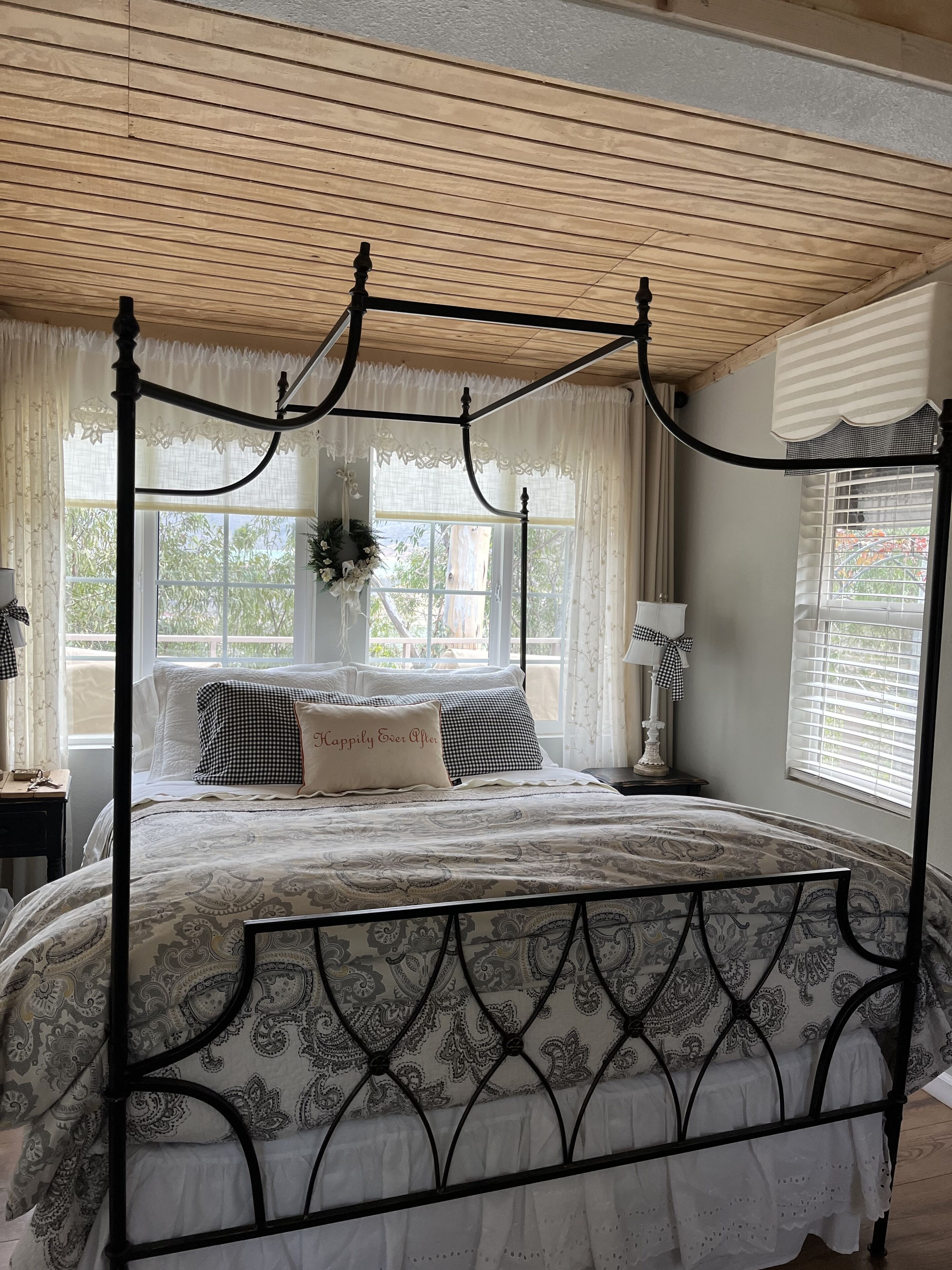 A four-poster bed with a patterned bedspread, a nightstand with a lamp, and a window with curtains.