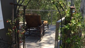 A wooden deck with a metal archway leading to a seating area with a cushioned chair and a small table.