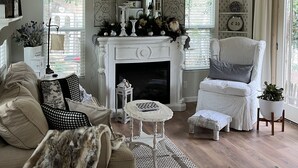A cozy living room with a fireplace, a chandelier, and a white armchair.