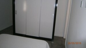 A room with a large wardrobe, a bed, and a door. - Condomínio Ed. Sirene Fraga (Guarapari)