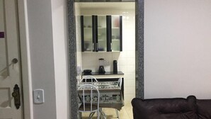 A kitchen with white cabinets, a coffee machine, and a dining table with chairs. - Condomínio Ed. Sirene Fraga (Guarapari)