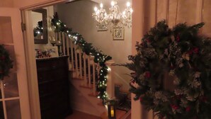 A staircase with a garland and a Christmas tree, a chandelier, and a mirror reflecting the room.
