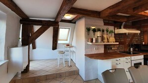 Eine kleine Küche mit sichtbaren Holzbalken, ein Essbereich mit Hockern und ein Fenster, das für natürliches Licht sorgt.