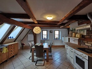 A kitchen with wooden beams, a dining table with chairs, a stove, and a window with a view.