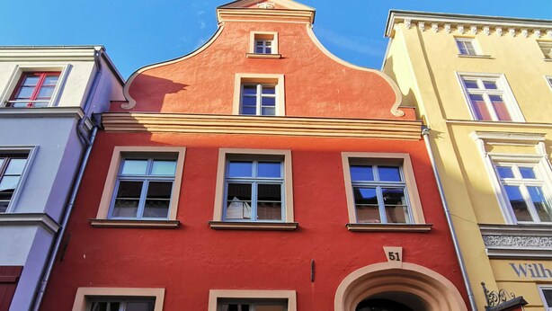 Ein rotes Gebäude mit mehreren Fenstern und einer grünen Tür, Hausnummer 51.