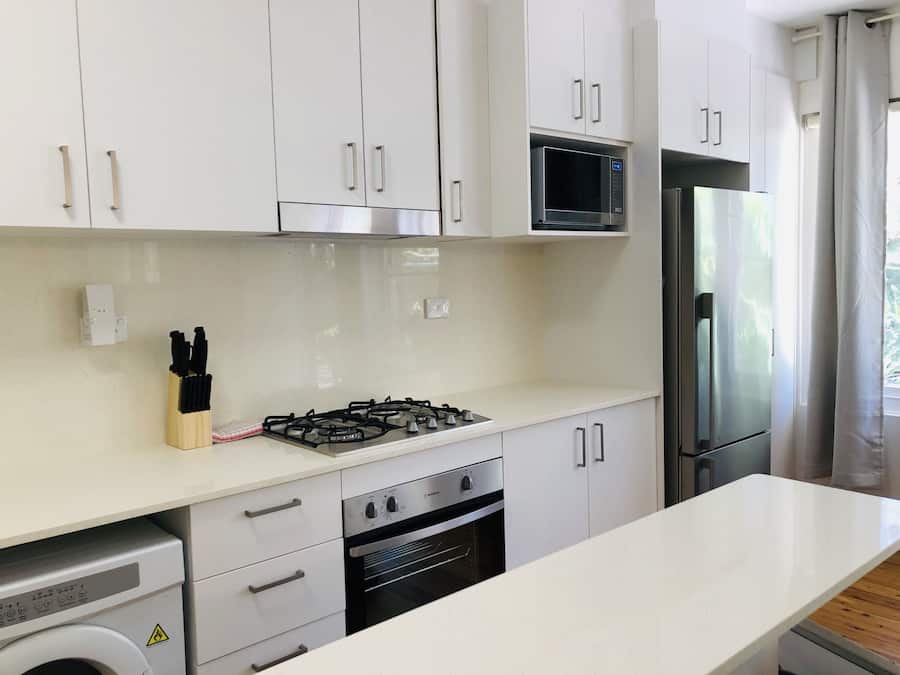 Una cocina moderna con armarios blancos, estufa a gas, horno, microondas y refrigerador.