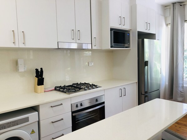 Una cocina moderna con armarios blancos, estufa a gas, horno, microondas y refrigerador.