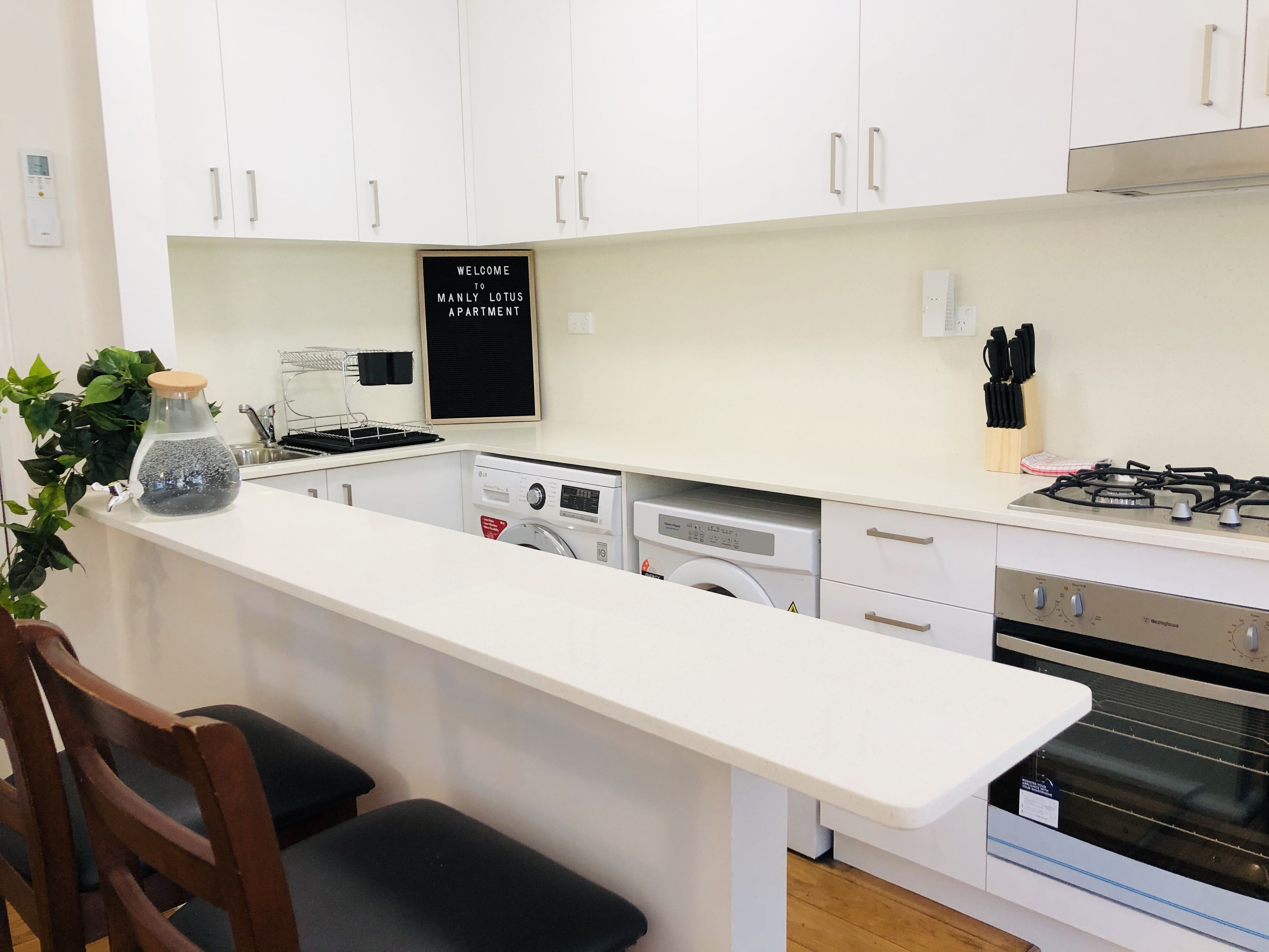 Une cuisine moderne avec des armoires blanches, un lave-linge encastré, une cuisinière à gaz et un tabouret de bar.