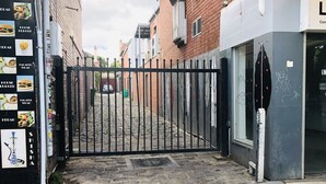 Un callejón amurallado con un edificio de ladrillo, un coche estacionado y un cartel con opciones de comida.