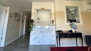 A reception area with a marble counter, a reception desk, a red vase with flowers, and a red and black patterned rug.