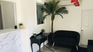 A living room with a black sofa, a small black table, a tall palm tree, and a white door.