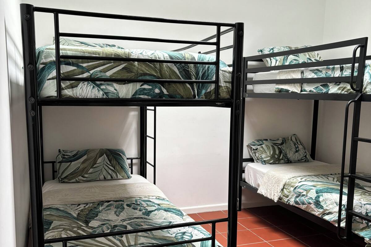 Une chambre avec un lit superposé et une couvre-lit ornée d’un motif de feuilles tropicales.