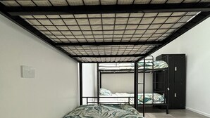 A dormitory room with bunk beds, a tiled ceiling, and a plain wall.