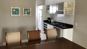 A dining area with a table and chairs, a kitchen with cabinets and appliances, and two wall-mounted paintings.