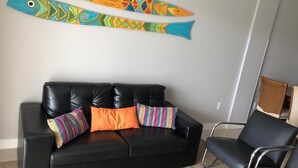 A black leather sofa with colorful striped pillows, a black chair, and a wall-mounted fish decoration.