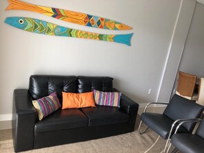 Relax in a stylish living room with a vibrant fish mural, a black leather sofa, and a cozy armchair.