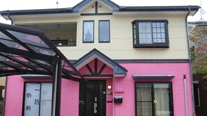 A two-story building with a pink facade and a black door. - Pop Culture House (Takayama)