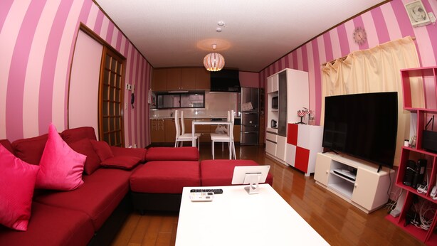 A living room with a red sofa, white coffee table, and a TV stand. - Pop Culture House (Takayama)