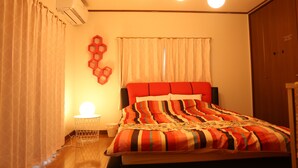 A bedroom with a bed, a bedside table, a wall-mounted air conditioner, a window with curtains, and a wooden wardrobe. - Pop Culture House (Takayama)