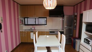 A kitchen with a white table and chairs, wooden cabinets, a stainless steel refrigerator, and a microwave. - Pop Culture House (Takayama)